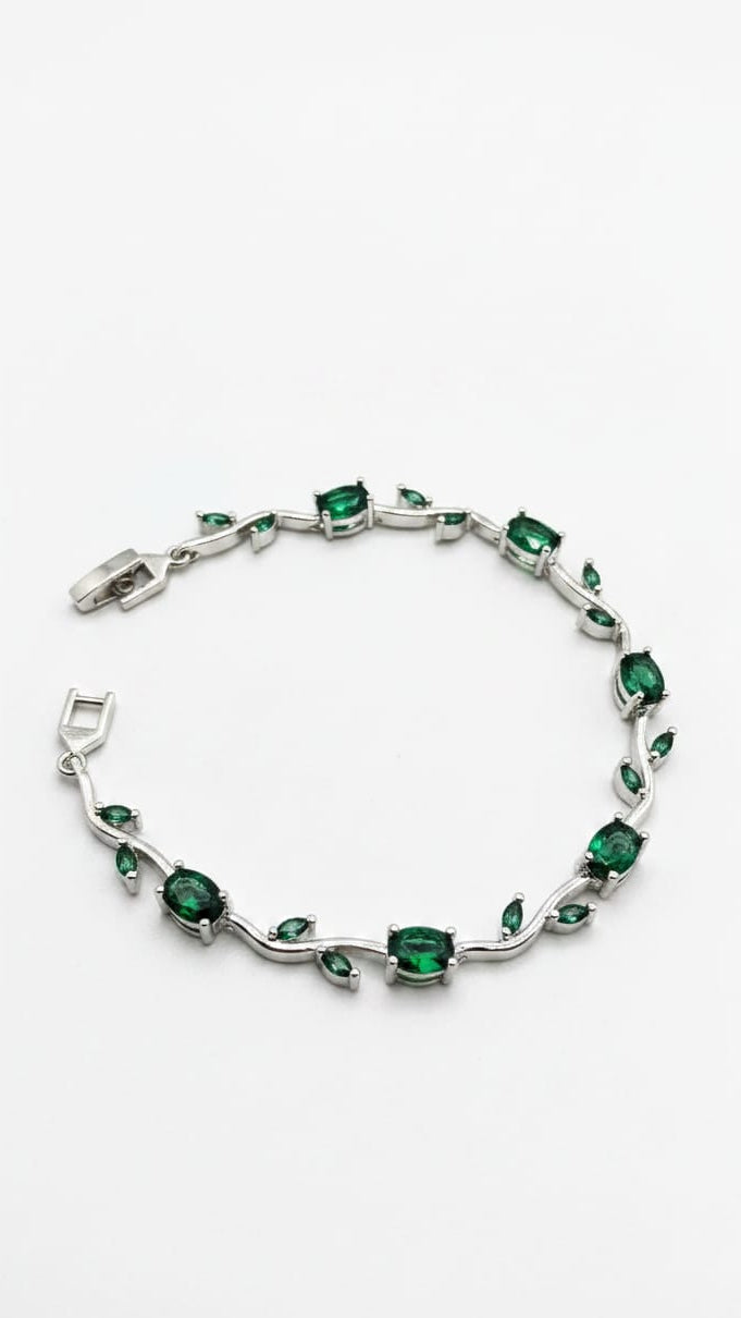 A silver-toned bracelet featuring green emerald-cut and marquise-cut gemstones arranged along a wavy vine design, displayed on a clean white background.
