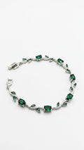 A silver-toned bracelet featuring green emerald-cut and marquise-cut gemstones arranged along a wavy vine design, displayed on a clean white background.